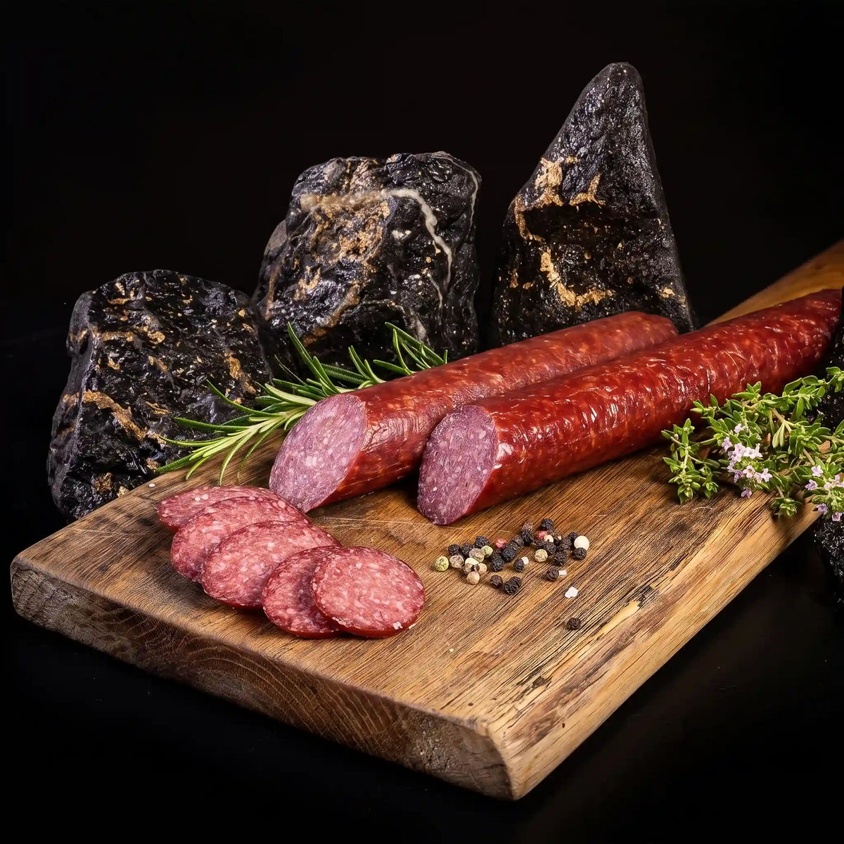 2 angeschnittene Salamis liegen auf einem rustikalen Holzbrett mit Steinhintergrund.
