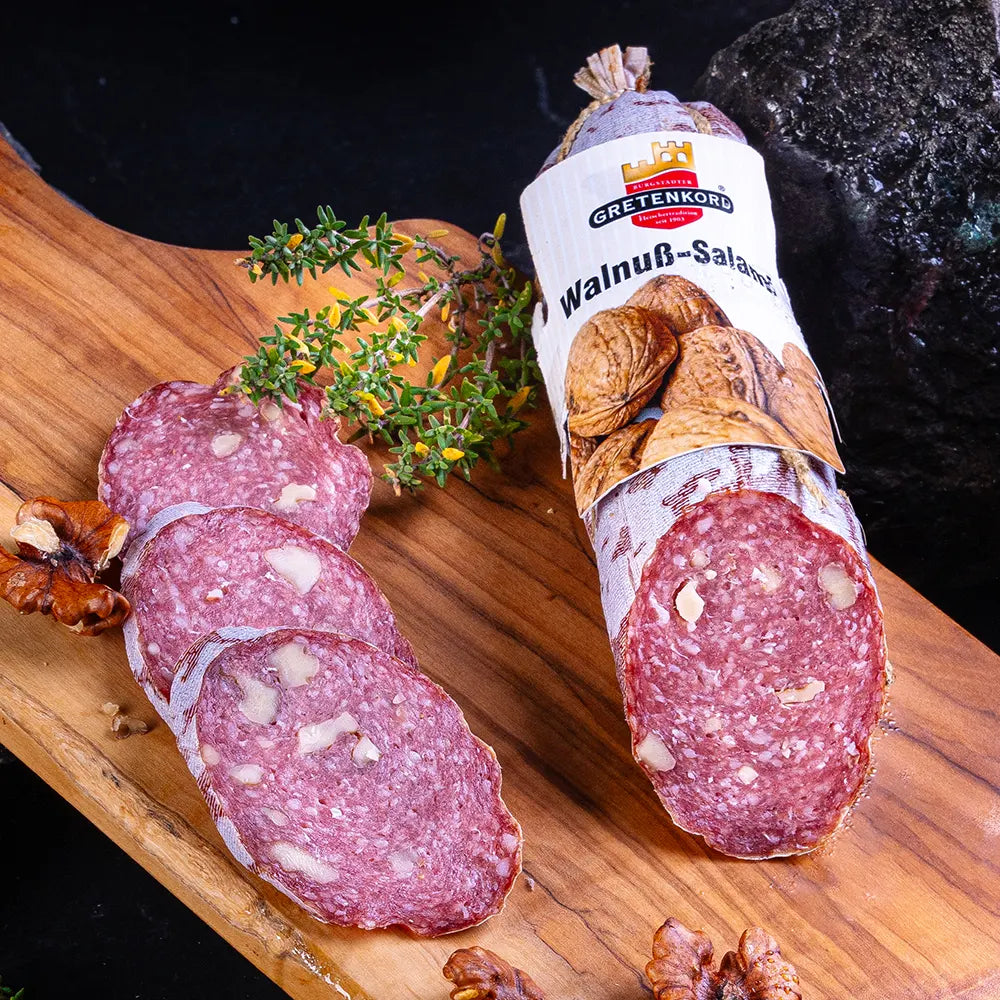 aufgeschnittene Salami mit Walnussstücken auf braunem Holzbrett