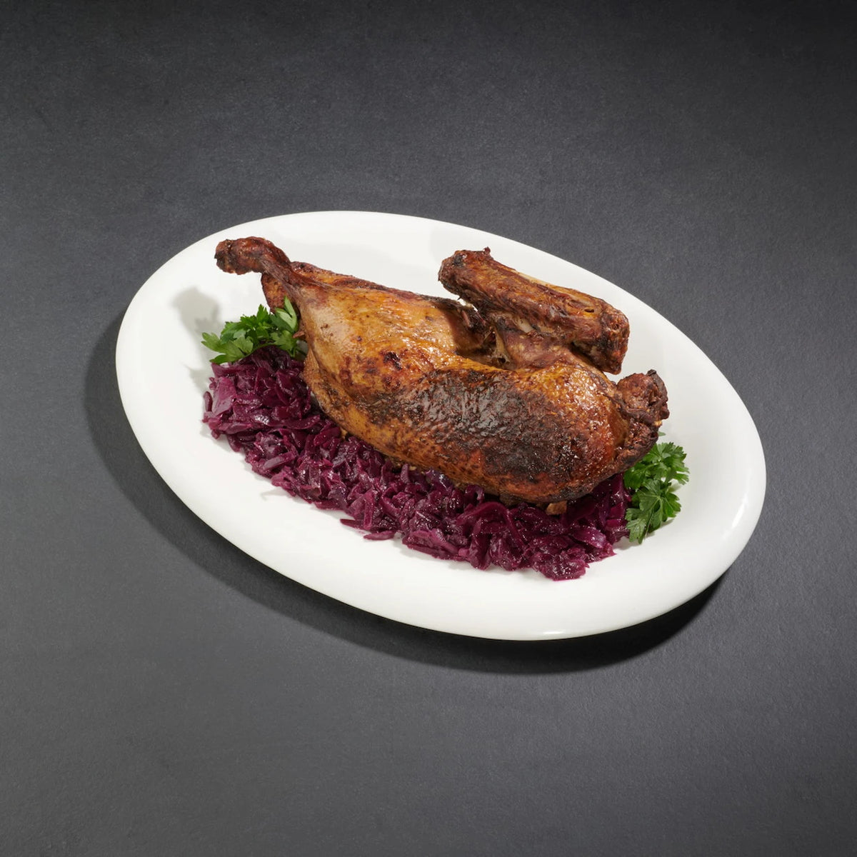 Eine halbe gegarte Ente angerichtet auf einem weißen Teller mit Rotkohl und Petersilie als Deko.