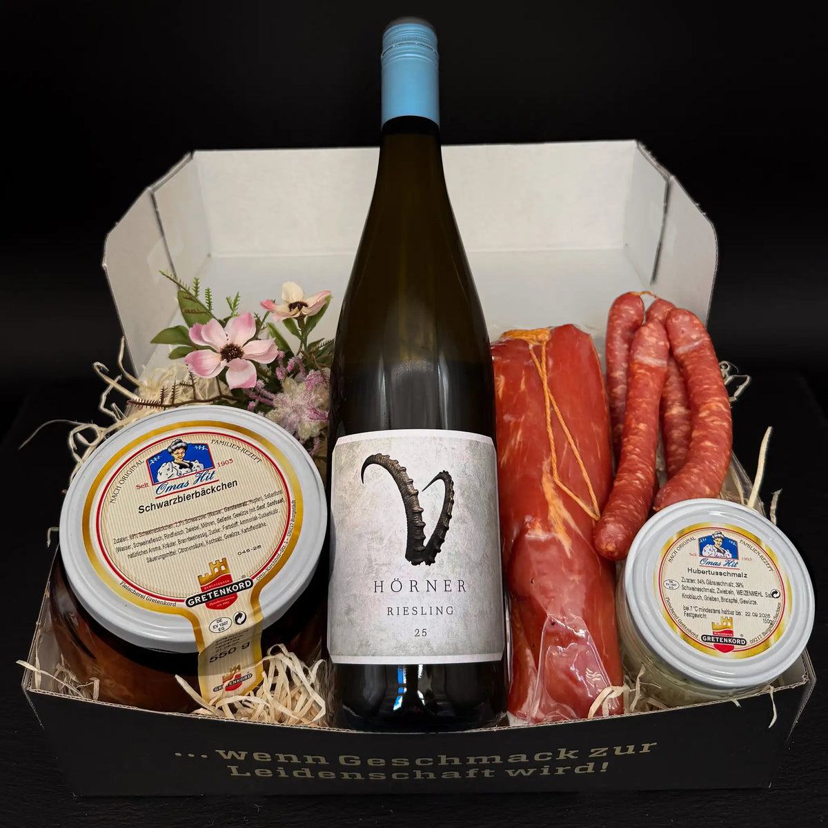Eine rechteckige Box gefüllt mit einem einem Glas Schwarzbierbäckchen und Hubertusschmalz, 2 Paar Pfefferbeißern, einem geräucherten Schweinefilet und eine Flasche Hörner Riesling.