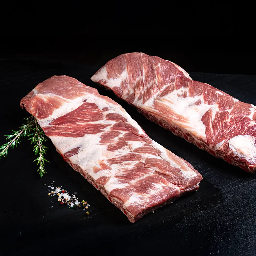 Zwei St. Louis Ribs vom Duroc Strohschwein von der Seite vor dunklem Hintergrund.