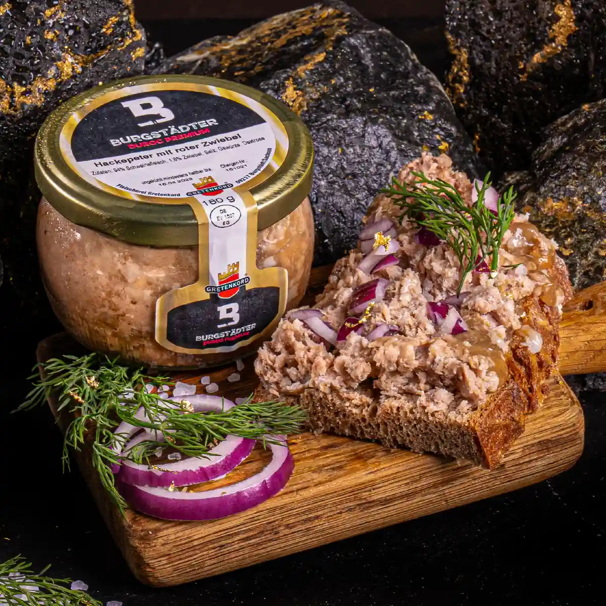 Ein Glas Hackepeter und daneben eine Scheibe Brot die damit bestrichen ist